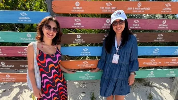 Duas mulheres posam sorrindo em frente a painel com nomes de famílias em barras coloridas em ilha da Disney