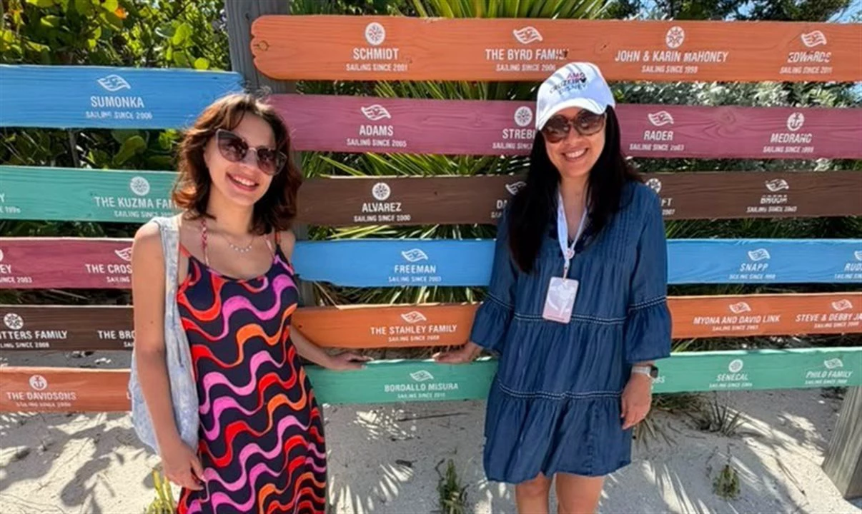Duas mulheres posam sorrindo em frente a painel com nomes de famílias em barras coloridas em ilha da Disney