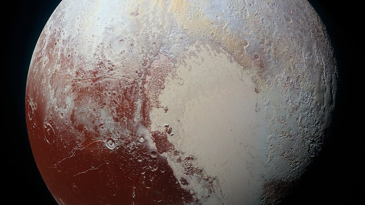 Plutão fotografado pela sonda New Horizons em 2015, mostrando a região em forma de coração com superfície clara e áreas avermelhadas, além de relevos e