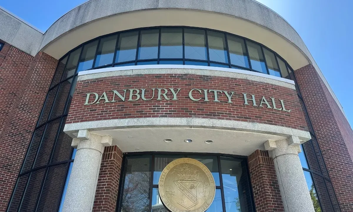 Fachada do Danbury City Hall, edifício de tijolos com grandes janelas curvas e brasão da cidade na entrada