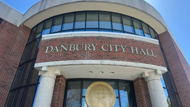 Fachada do Danbury City Hall, edifício de tijolos com grandes janelas curvas e brasão da cidade na entrada