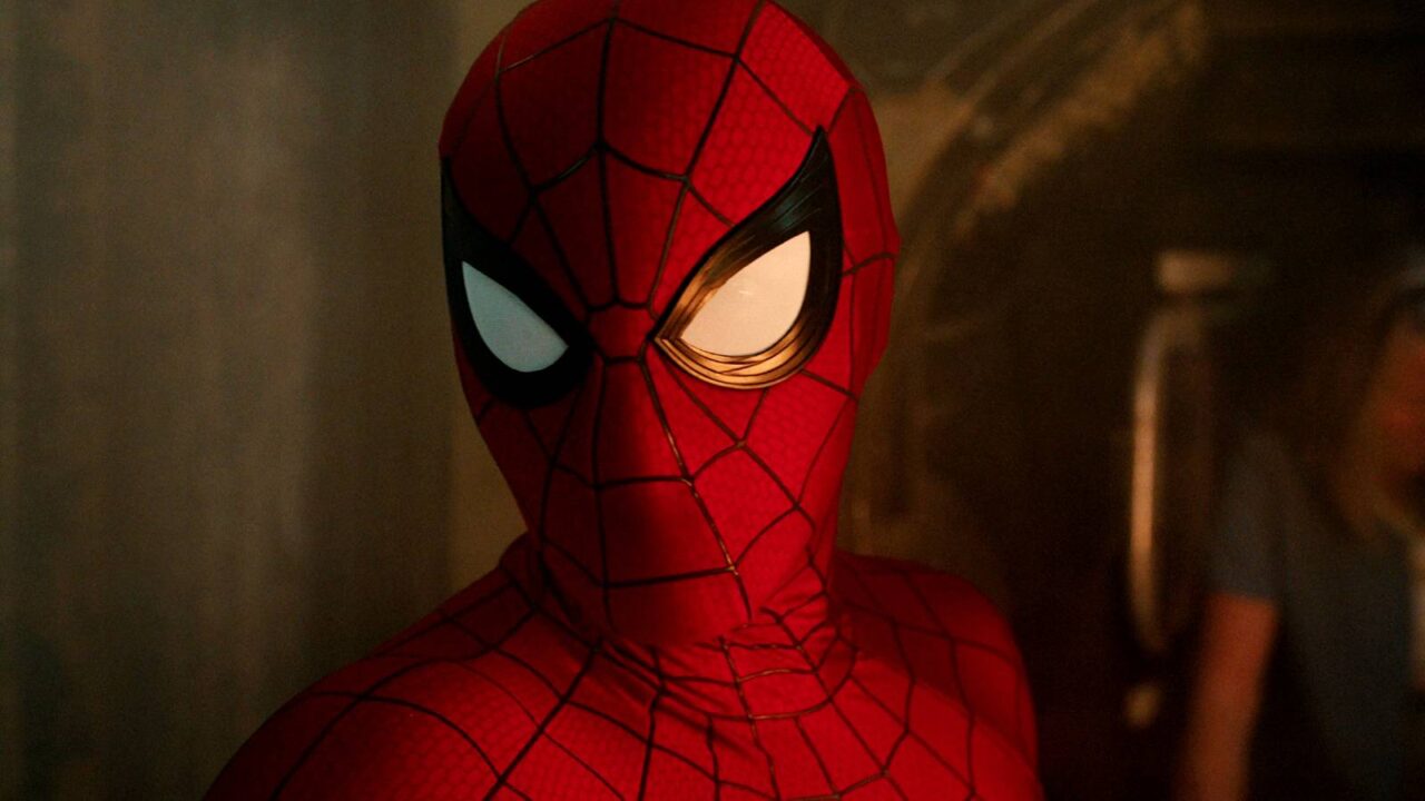 Personagem em traje vermelho com padrão de teia em ambiente fechado com iluminação dramática