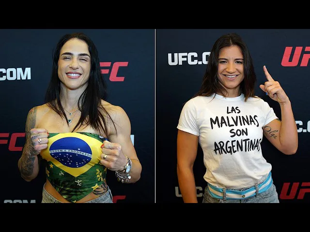 Duas mulheres em evento do UFC posam para fotos em frente a painel de patrocinadores, uma exibindo bandeira do Brasil e a outra usando camiseta com mensagem sobre Argentina