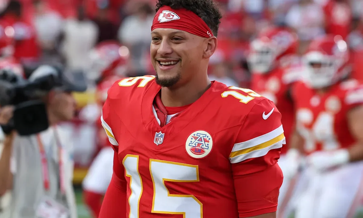 Jogador de futebol americano com uniforme vermelho e branco sorri durante partida no estádio, com torcedores ao fundo