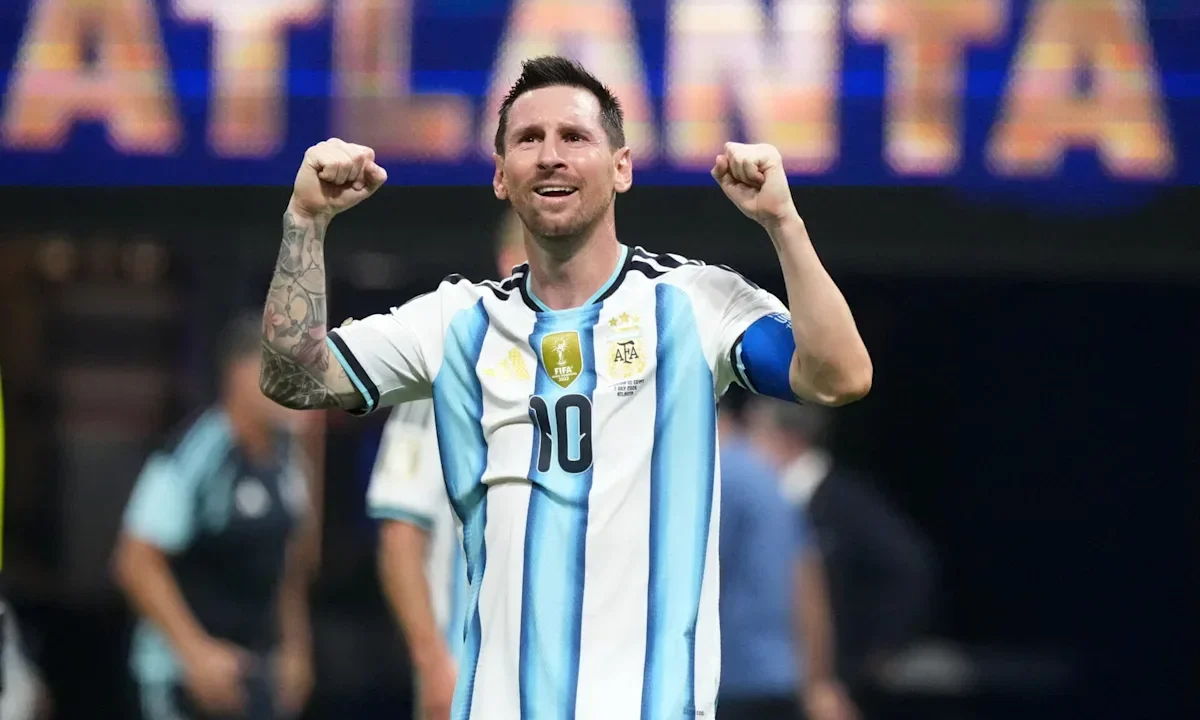 Jogador da seleção argentina com número 10 levanta os punhos em comemoração durante partida em estádio, com placa ao fundo exibindo texto em inglês