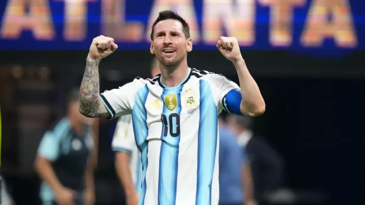 Jogador da seleção argentina com número 10 levanta os punhos em comemoração durante partida em estádio, com placa ao fundo exibindo texto em inglês