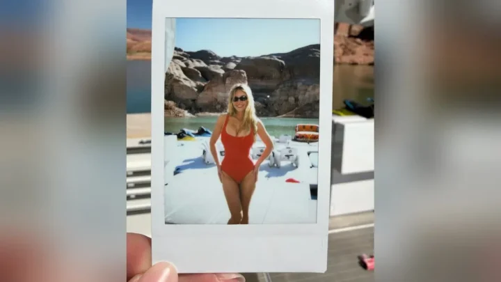 Foto instantânea mostra mulher de maiô vermelho e óculos escuros posando à beira de lago com montanhas rochosas e água azul-turquesa ao fundo