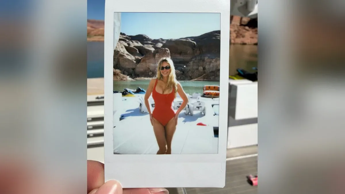 Foto instantânea mostra mulher de maiô vermelho e óculos escuros posando à beira de lago com montanhas rochosas e água azul-turquesa ao fundo