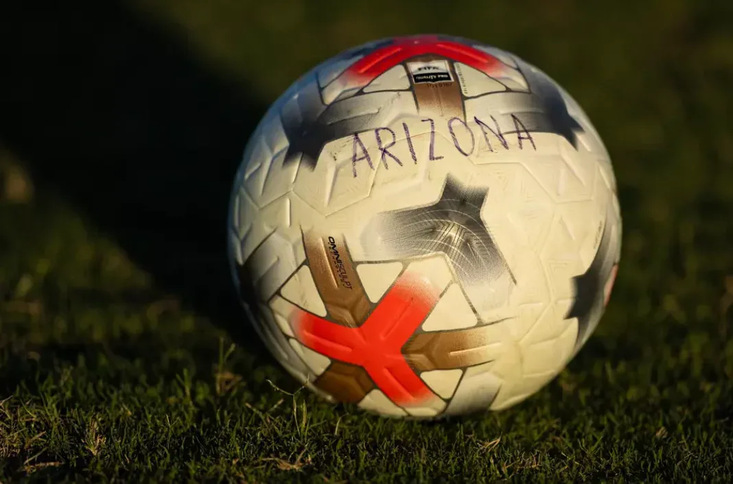 Bola de futebol com logotipo da Arizona sobre grama em estádio, durante partida entre universidades