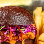 Devilish Crispy Chicken Sandwich: maionese apimentada, repolho roxo e pimenta Fresno em pão kaiser preto, servido com batatas fritas