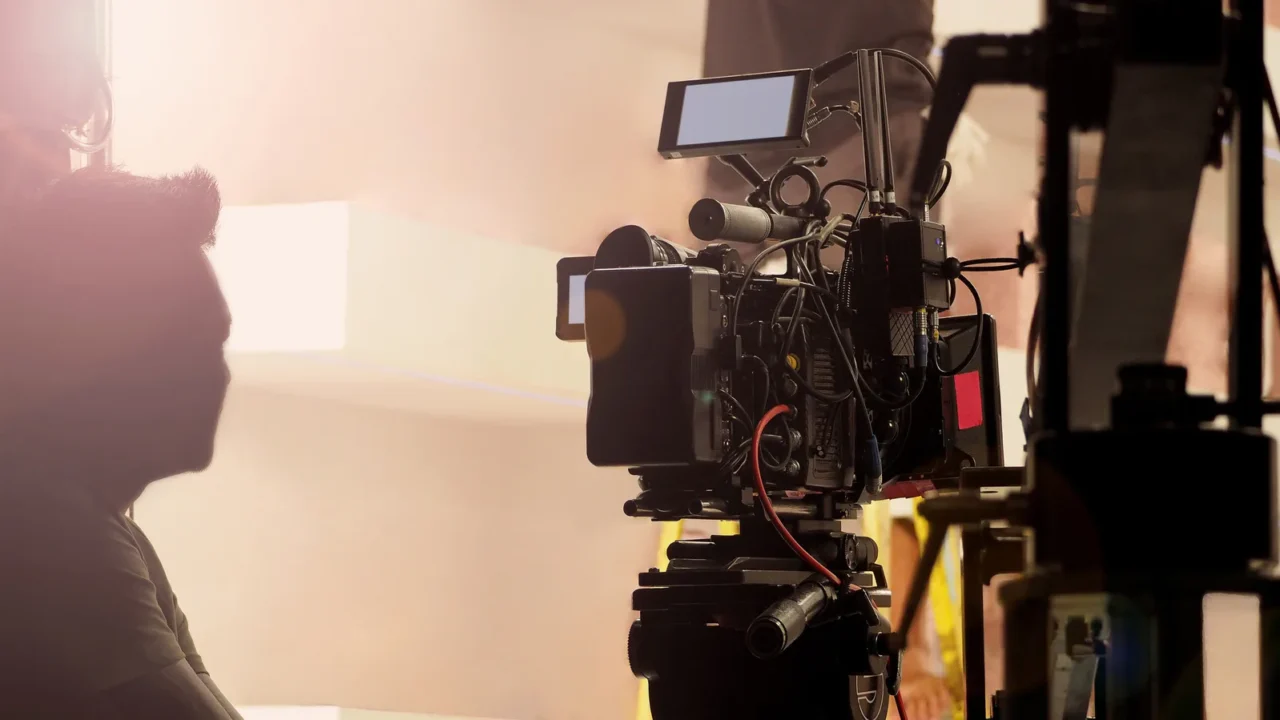 Câmera profissional de cinema com múltiplos monitores e microfones acoplados em set de gravação com iluminação ambiente