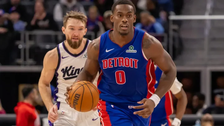 Jogador do Detroit em uniforme azul conduz a bola enquanto é marcado por adversário do Sacramento em partida de basquete da NBA