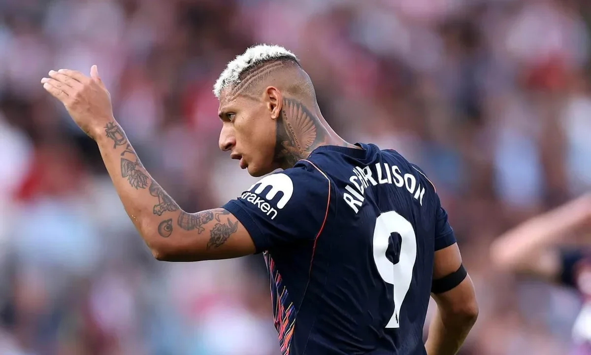 Jogador de futebol com a camisa número 9 gesticula durante partida em estádio com público ao fundo
