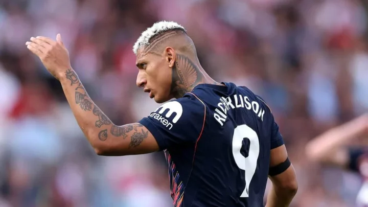 Jogador de futebol com a camisa número 9 gesticula durante partida em estádio com público ao fundo