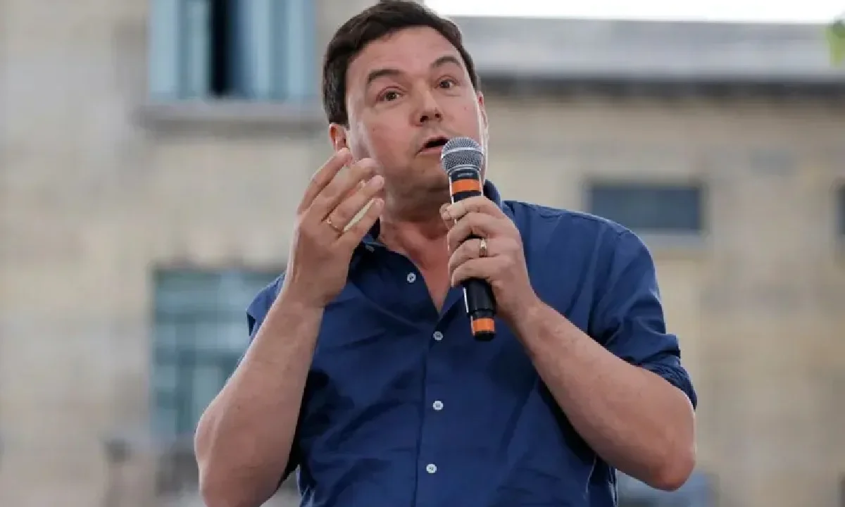 Homem de camisa azul fala ao microfone durante apresentação em espaço aberto, gesticulando com as mãos enquanto apresenta seu ponto de vista