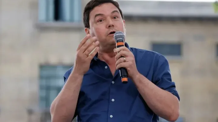 Homem de camisa azul fala ao microfone durante apresentação em espaço aberto, gesticulando com as mãos enquanto apresenta seu ponto de vista