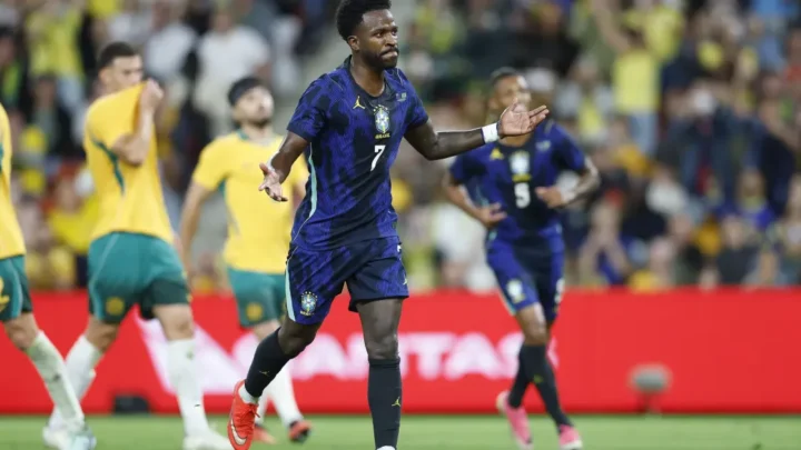 Jogador da seleção brasileira com uniforme azul durante partida contra seleção em amarelo e verde, em estádio com público