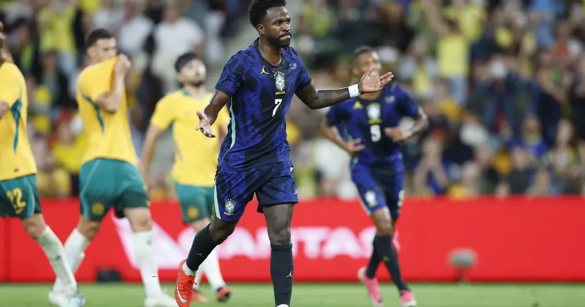 Jogador da seleção brasileira com uniforme azul durante partida contra seleção em amarelo e verde, em estádio com público