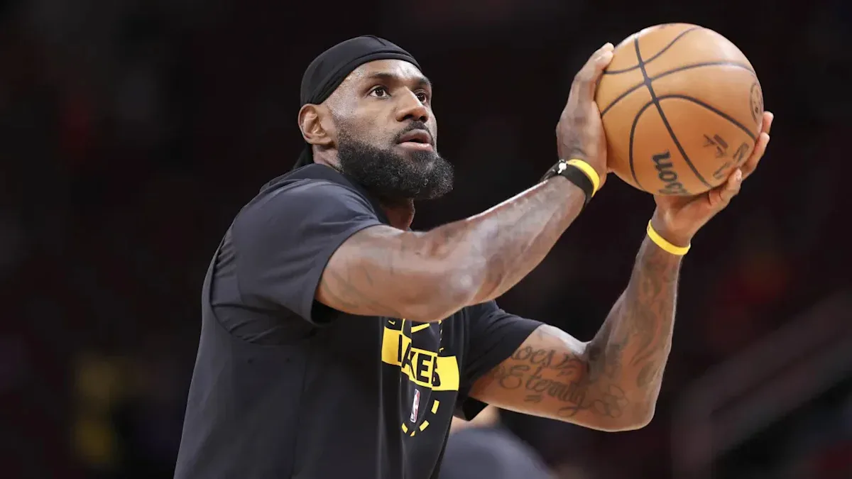 Jogador de basquete em uniforme preto e amarelo prepara-se para fazer um arremesso durante partida, com foco e concentração