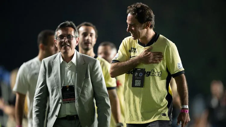 Homem de terno e óculos conversa com jogador em uniforme amarelo durante evento em campo noturno