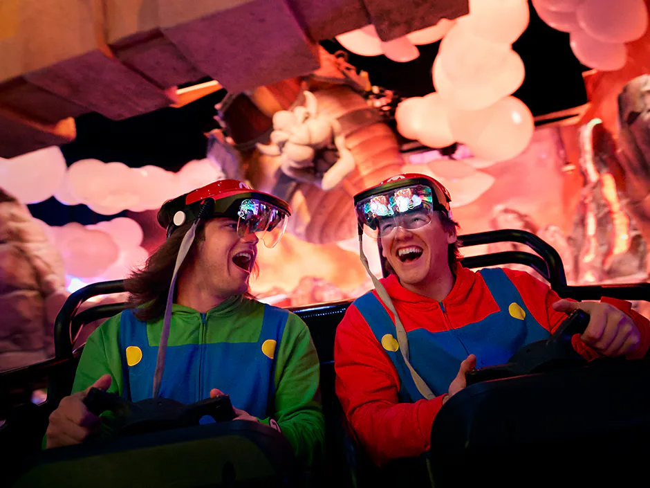 Dois meninos sorriem e riem um para o outro enquanto andam no Mario Kart: Bowser's Challenge no Universal Epic Universe