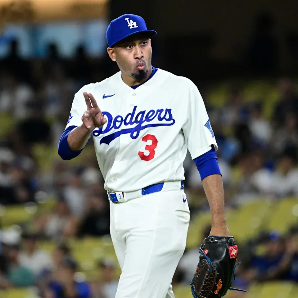 Jogador do Dodgers com uniforme branco e número 3 gesticula durante jogo de beisebol em estádio com público nas arquibancadas