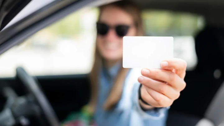 Pessoa dentro de veículo segura e exibe nova carteira de motorista com documento em branco visível na mão