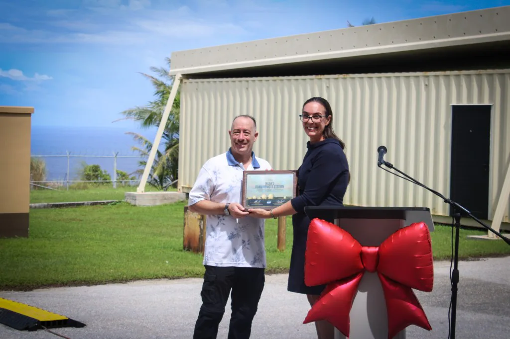 Jena Garrahy (à direita), vice-gerente de Operações de Rede do SCaN, entrega um certificado de reconhecimento ao gerente do local da Estação Remota de Guam, Kristopher Copple (à esquerda).