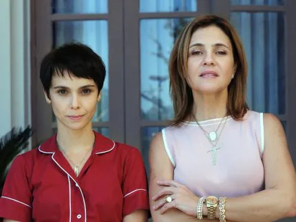 Duas mulheres posam em ambientes internos com vidraças ao fundo
