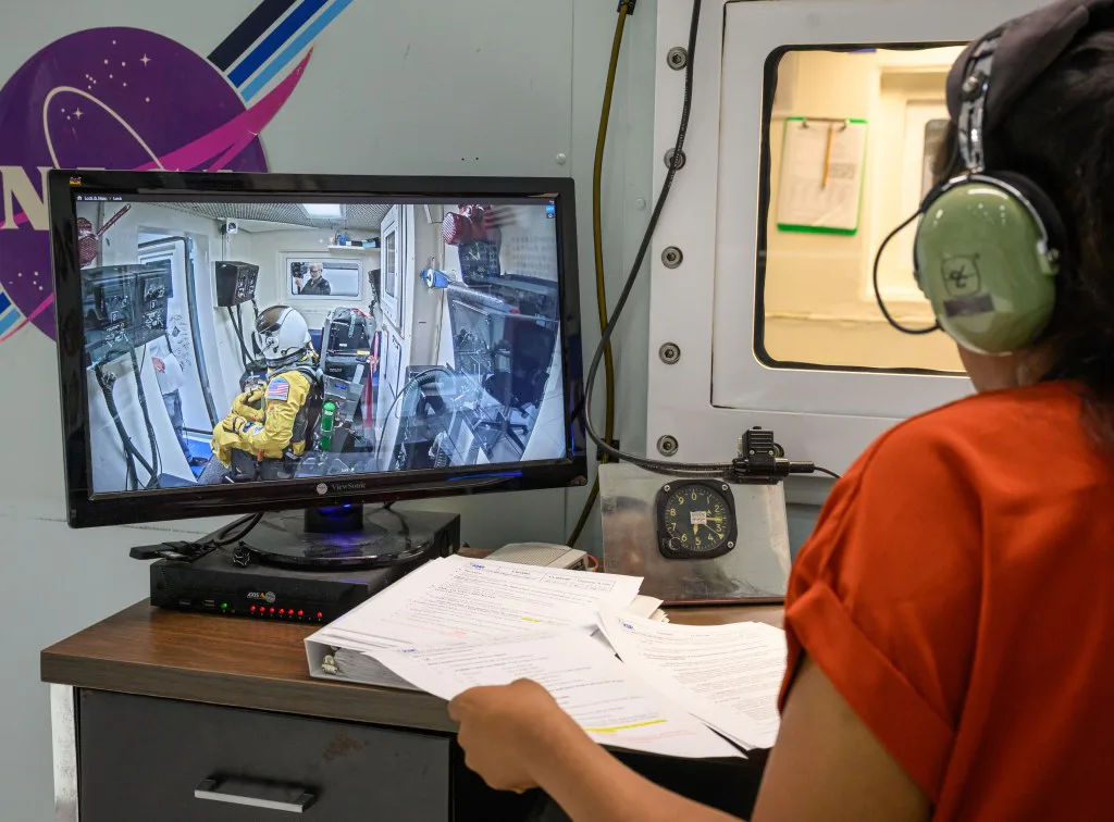 Um membro da equipe da NASA observa o candidato a astronauta Adam Fuhrmann enquanto ele completa uma sessão em câmara de altitude.