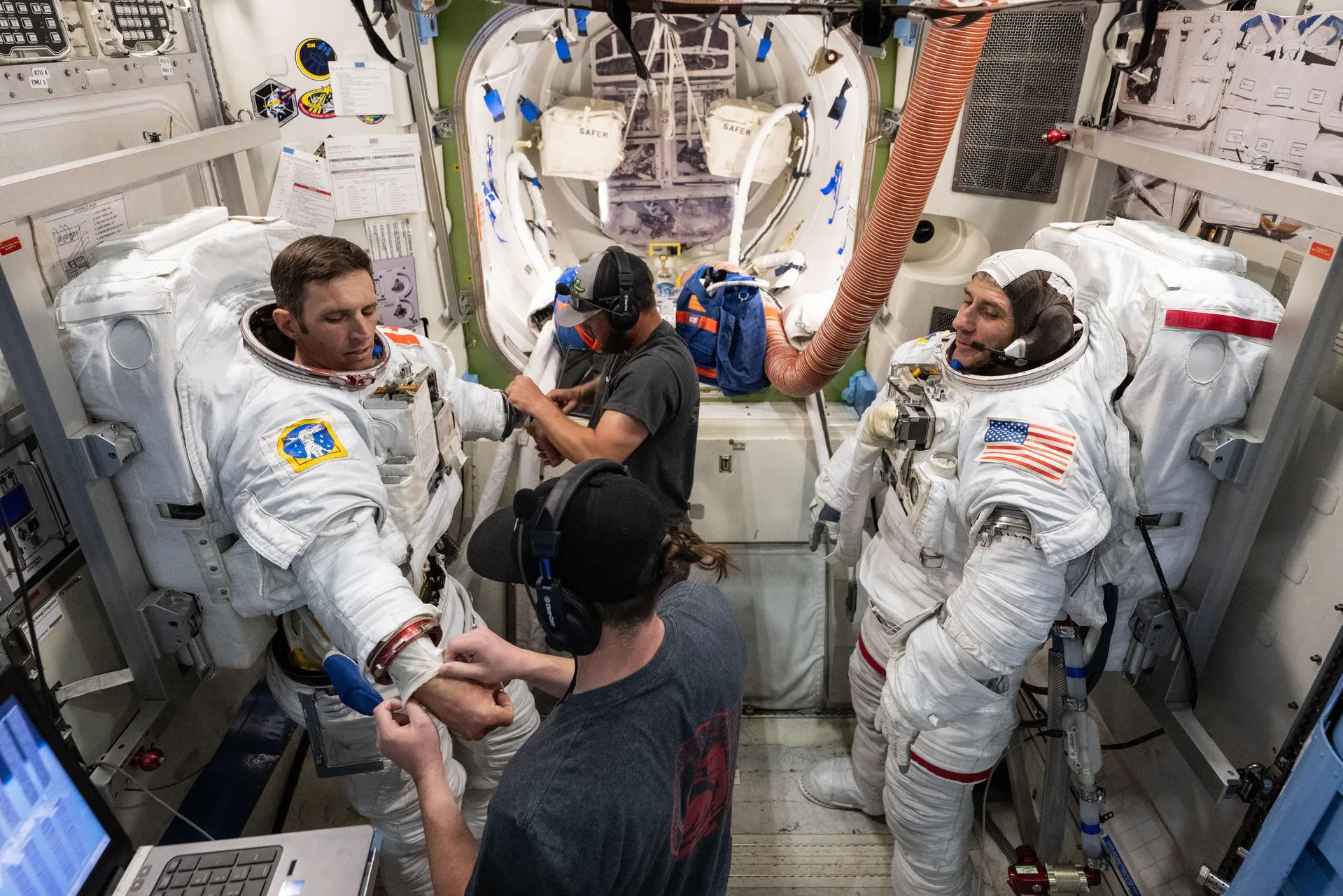O astronauta da CSA (Agência Espacial Canadense) Josh Kutryk (à esquerda) e o astronauta da NASA Luke Delaney (à direita), com auxílio de especialistas em treinamento, praticam a colocação de trajes espaciais em um simulador de câmara de descompressão da Estação Espacial Internacional na Instalação de Maquetes de Veículos Espaciais do Centro Espacial Johnson (JSC), em Houston, Texas. Os astronautas se familiarizam com os sistemas e procedimentos dos trajes espaciais e praticam as operações da câmara de descompressão Quest antes de realizar treinamento de caminhada espacial no Laboratório de Flutuabilidade Neutra do JSC, em microgravidade simulada.