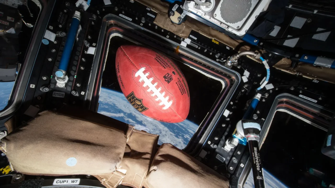 Uma bola de futebol americano flutua em microgravidade a bordo da Estação Espacial Internacional, bem acima da Terra.
