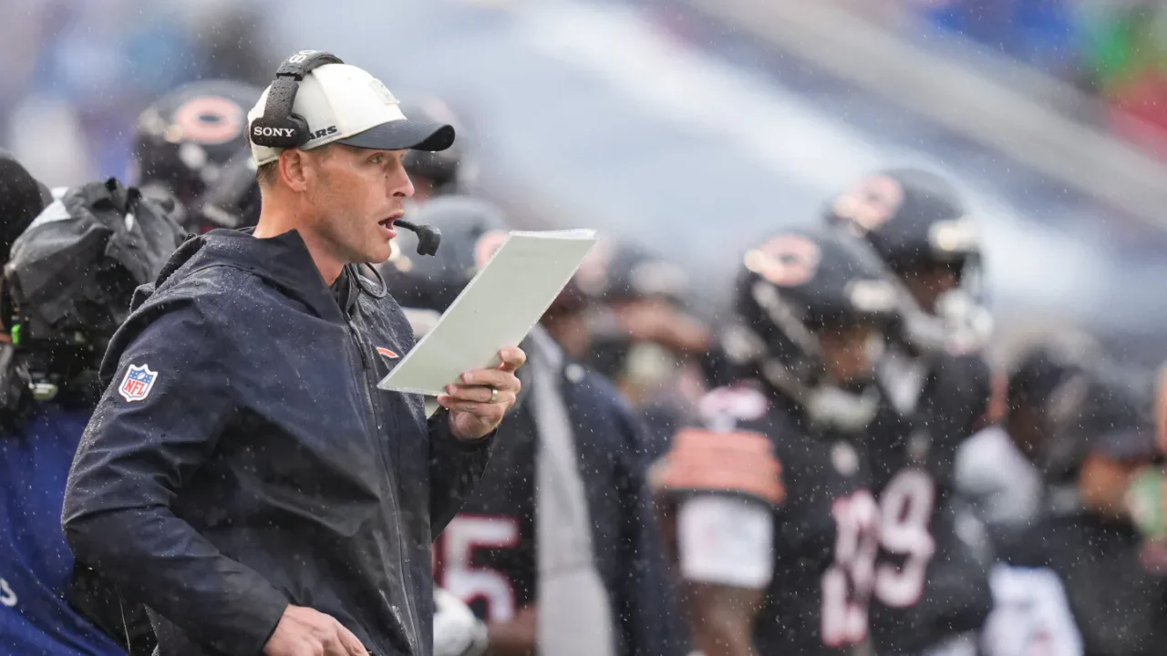 Treinador com boné e fone de ouvido segura tablet enquanto comanda estratégias em jogo de futebol americano sob chuva