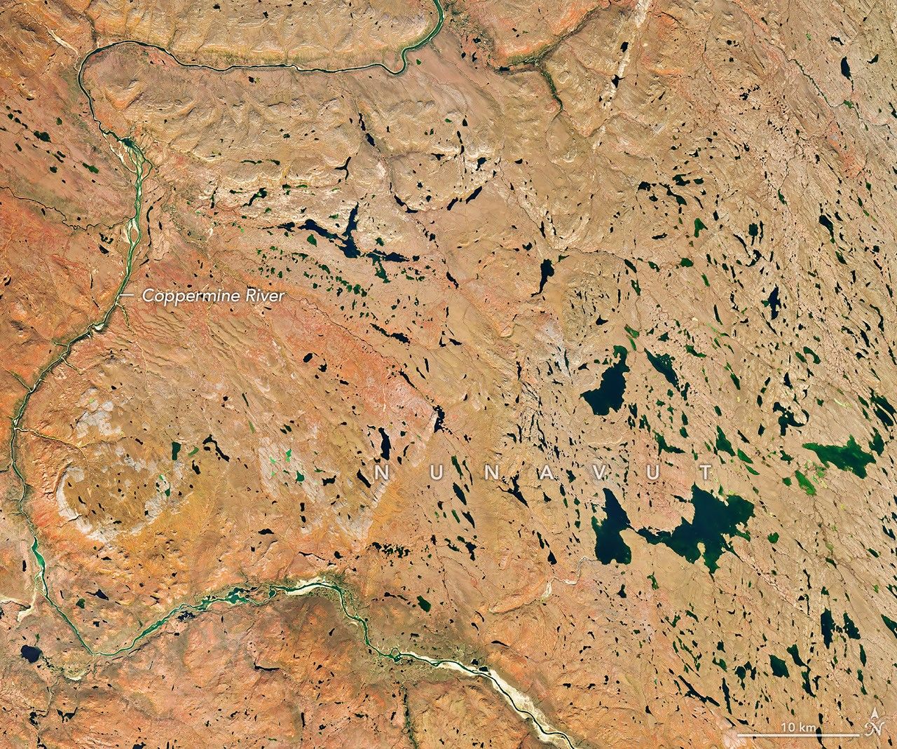 Um rio serpenteia pela mesma paisagem de tundra no outono, agora colorida de vermelho e laranja. Um pouco de vegetação verde ainda é visível ao longo do rio.