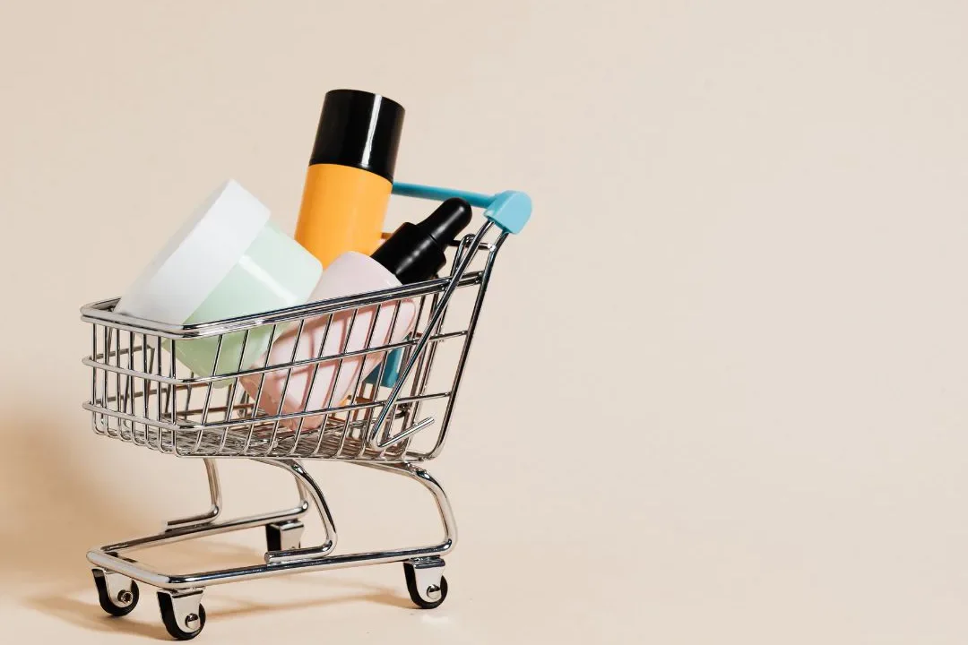 Carrinho de compras em miniatura contém produtos de beleza e higiene pessoal contra fundo bege