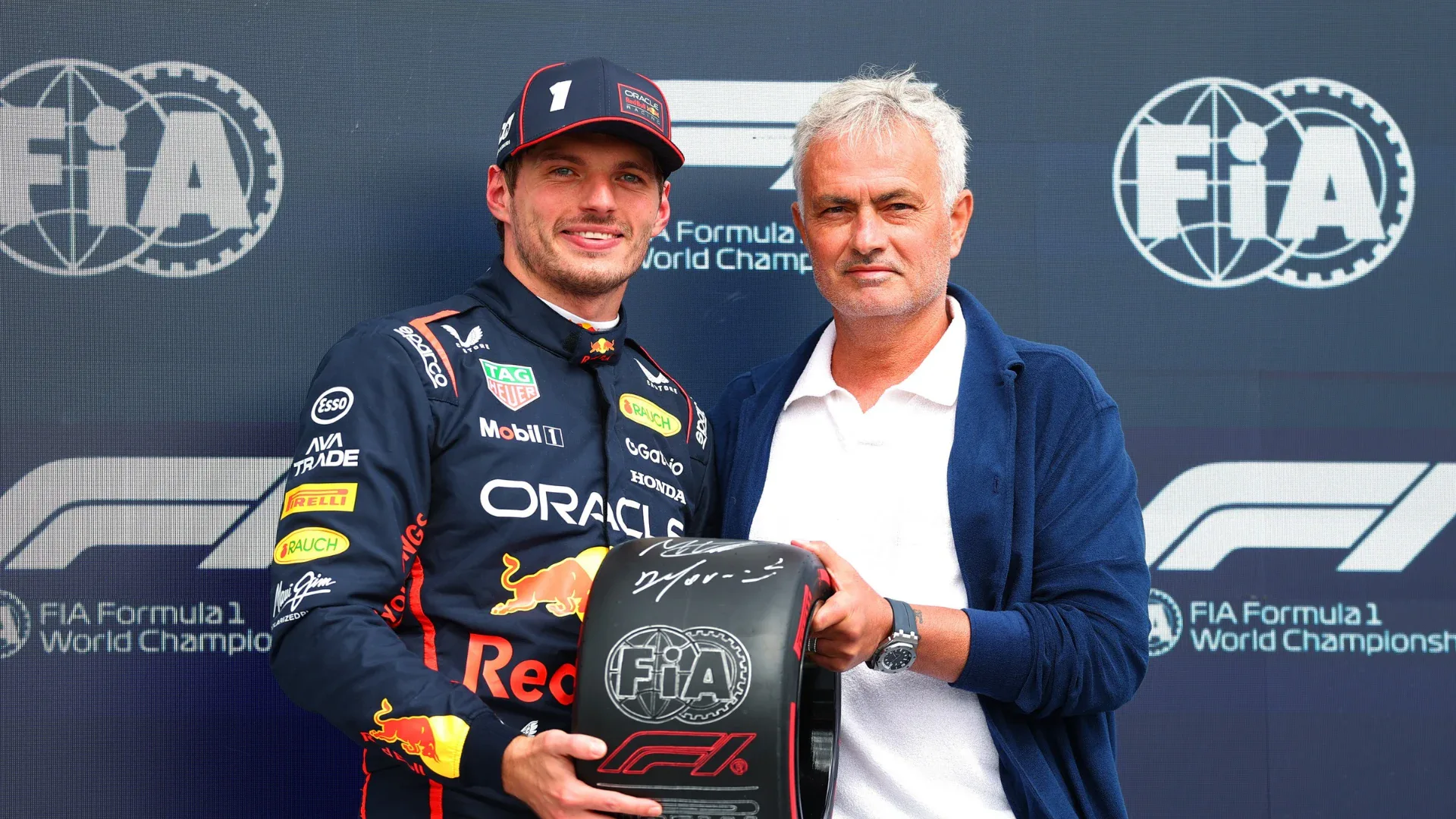 Técnico de futebol posa com piloto de Fórmula 1 durante solenidade no Grande Prêmio da Espanha, ambos segurando troféu com emblema da FIA