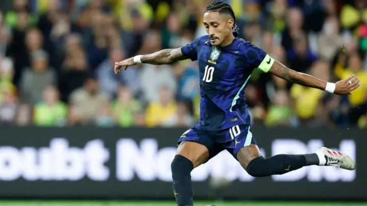Jogador da Seleção Brasileira com número 10 e braçadeira de capitão controla a bola durante partida em estádio com público ao fundo