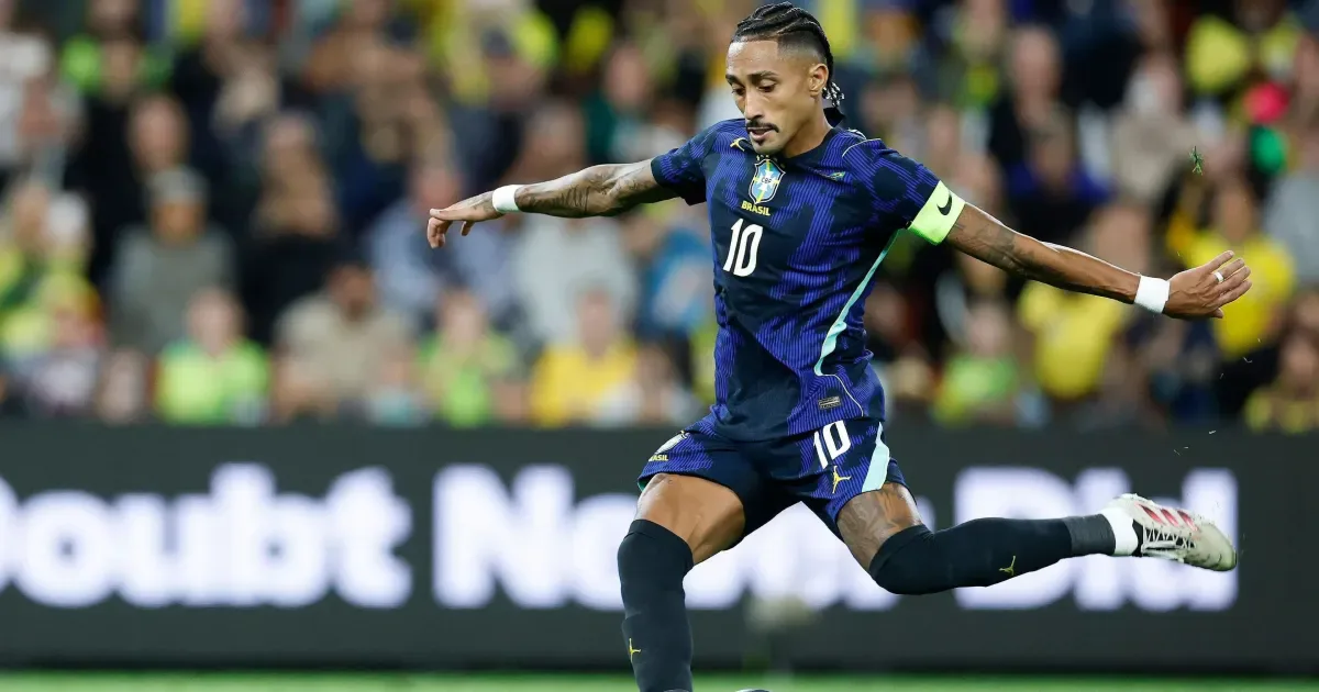 Jogador da Seleção Brasileira com número 10 e braçadeira de capitão controla a bola durante partida em estádio com público ao fundo