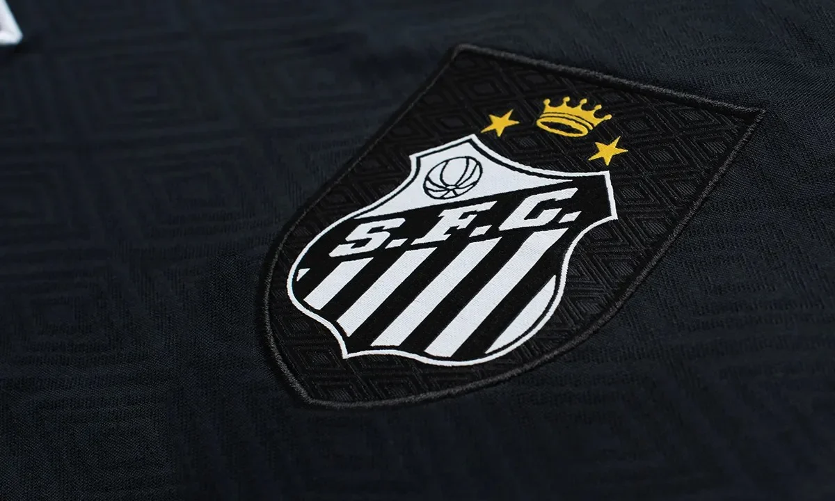 Detalhe do escudo e da gola de camisa preta com listras brancas verticais, exibindo coroa e estrelas em dourado na parte superior do brasão