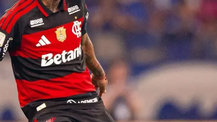 Jogador em uniforme vermelho e preto com patrocínio de casa de apostas durante partida de futebol