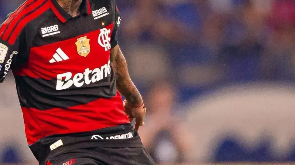 Jogador em uniforme vermelho e preto com patrocínio de casa de apostas durante partida de futebol