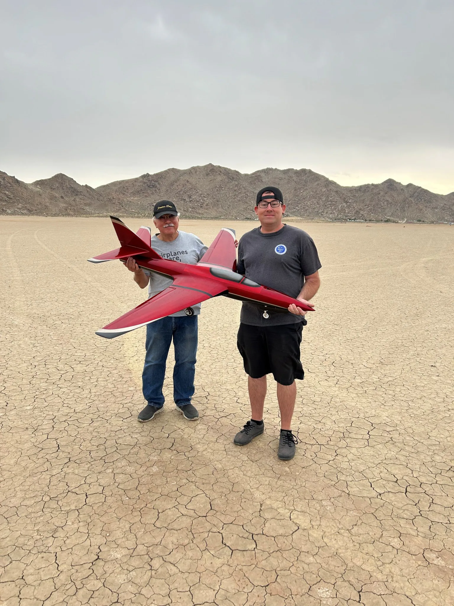 Justin Link, piloto de drones do Laboratório de Pesquisa de Voo em Escala Reduzida Dale Reed, no Centro de Pesquisa de Voo Armstrong da NASA, em Edwards, Califórnia, e seu pai, Don Link, seguram uma aeronave controlada por rádio Firebird no dia de seu primeiro voo. Foi um projeto em que trabalharam juntos. Don Link reduziu as dimensões do modelo original de escala maior e desenhou os planos, enquanto Justin Link fabricou os moldes compostos e construiu a aeronave do zero.
