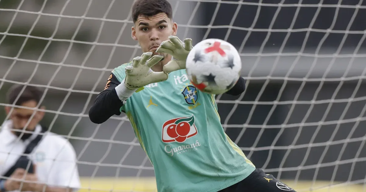 Goleiro da seleção brasileira realiza defesa durante treinamento ou partida, posicionado na frente da meta com as mãos estendidas para aparar a bola