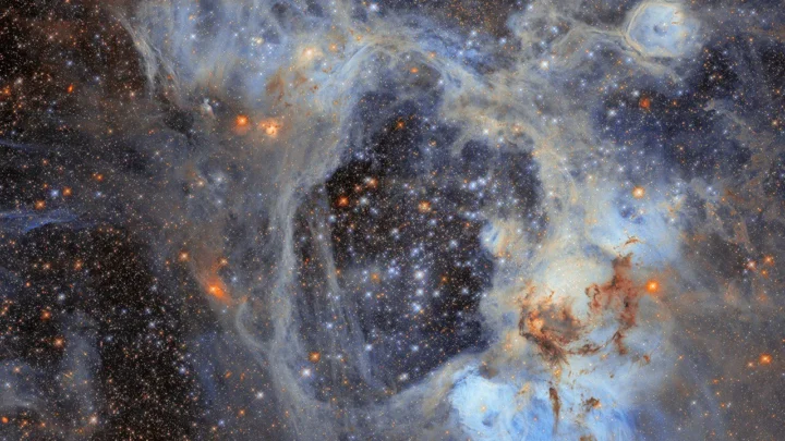 Imagem de telescópio espacial mostrando a nebulosa N44, com estruturas gasosas azuladas e brancas entrelaçadas, aglomerados de estrelas em laranja e azul, e regiões de gás aquecido formando padrões sinuosos contra o fundo do espaço escuro