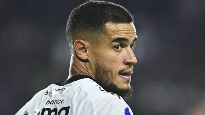 Jogador de futebol com uniforme branco de clube brasileiro com patrocínio de banco durante partida noturna