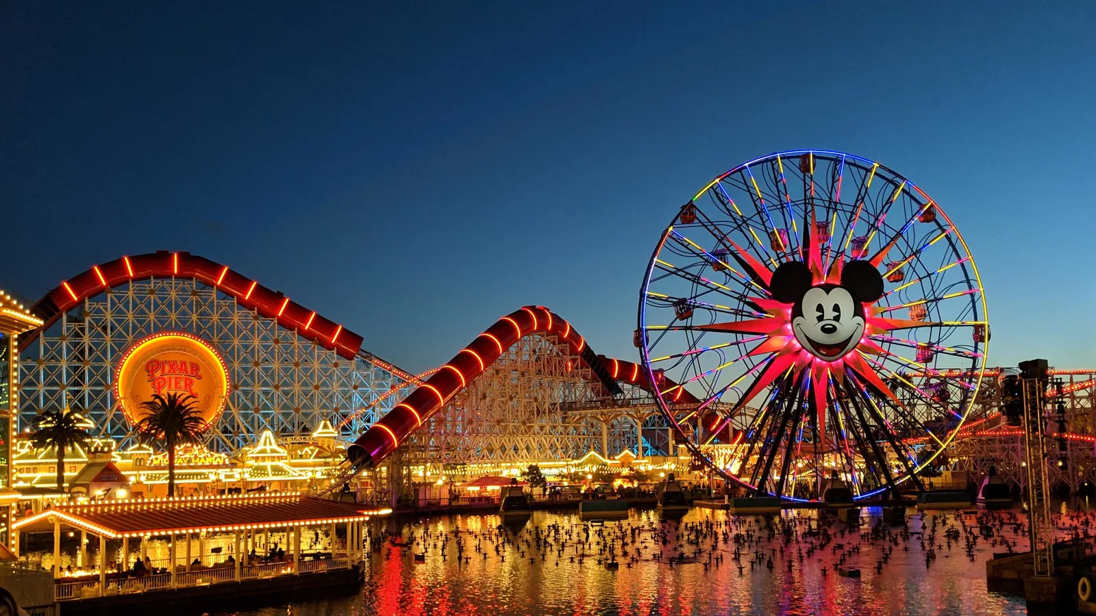 Foto de arquivo de 2019 do Pixar Pier ao entardecer, com a Incredicoaster e a roda-gigante do Mickey iluminadas e refletidas no lago