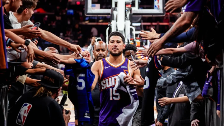 Jogador do Phoenix Suns, de camisa roxa e número 15, caminha por corredor ladeado por torcedores que estendem braços, camisas e canetas para autógrafos