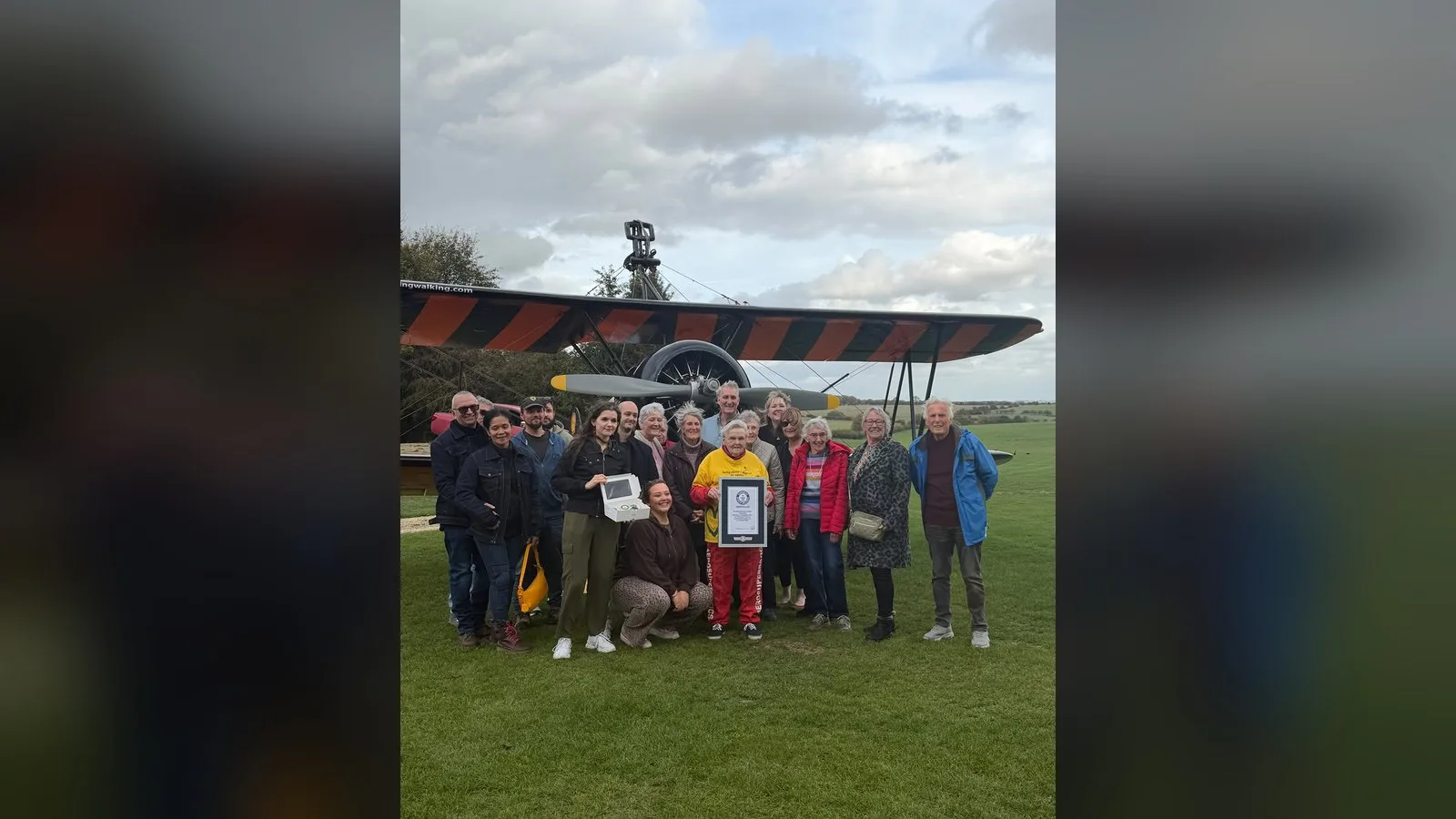 Helga Duffy posa com familiares e amigos no gramado do aeródromo, com o biplano ao fundo