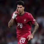 Jogador em uniforme de seleção europeia vermelha na número 20 durante partida de futebol em estádio com público ao fundo