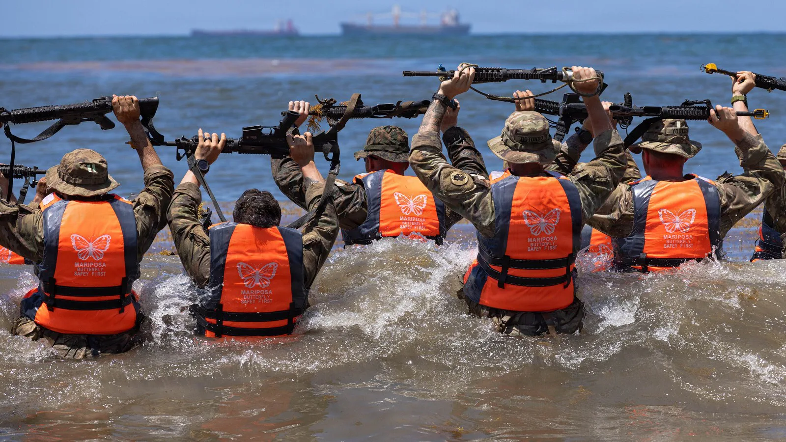 Militares americanos e panamenhos com coletes salva-vidas laranja erguem os fuzis acima da cabeça dentro da água, durante treino de operações aquáticas do curso de selva no Panamá, em março de 2026